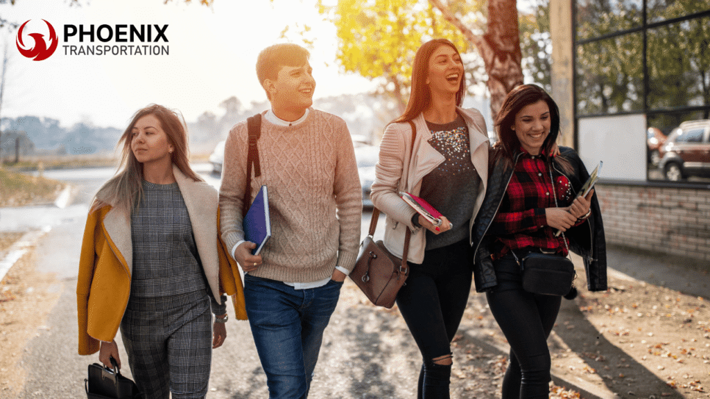 A group of four smiling young adults walks down a sunlit street, holding books and bags. They're dressed in casual autumn attire, exuding warmth and camaraderie.