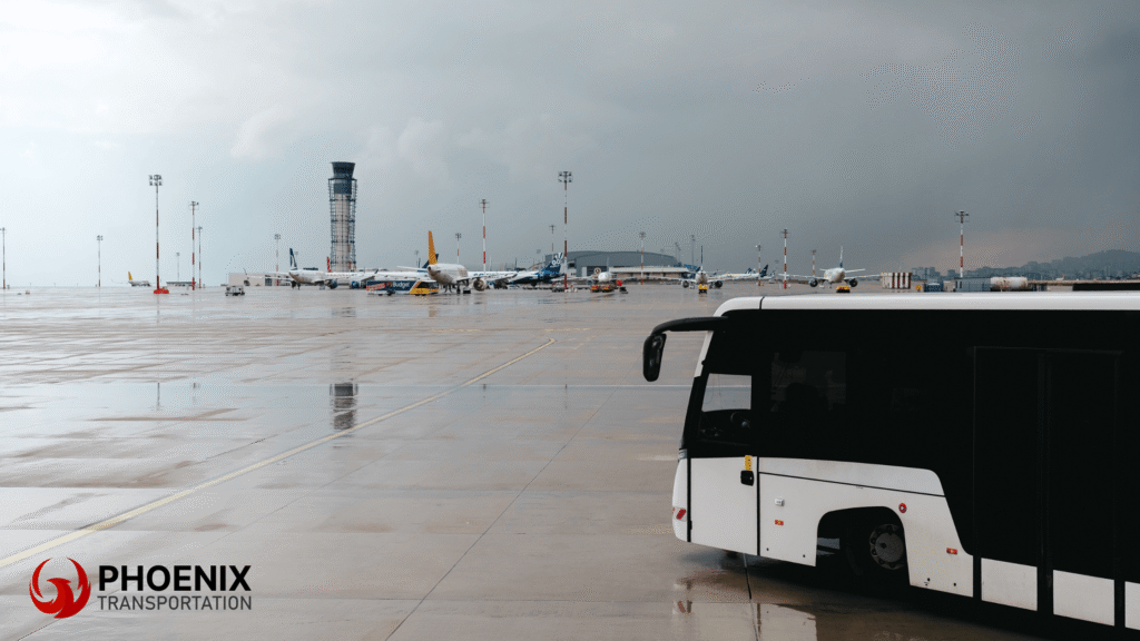 A white bus on a wet san jose airport tarmac with airplanes and a control tower in the background during a storm