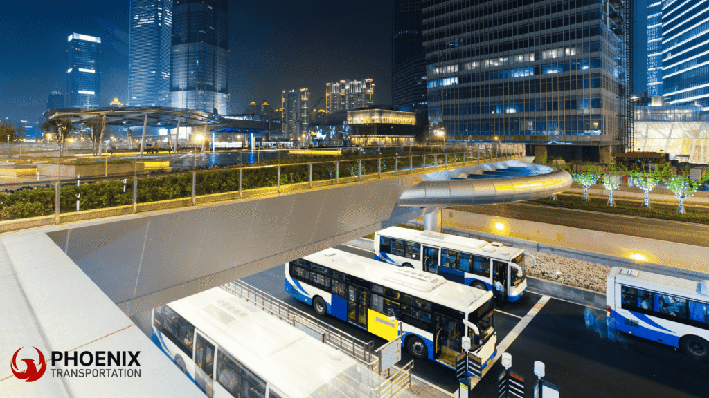 Night cityscape with modern buildings illuminated, featuring a public transit hub with parked buses below a bridge.