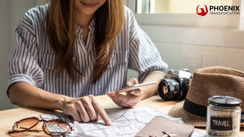 Woman planning bus travel in Oakland at a wooden table with a map, phone, camera, and travel essentials in daylight.